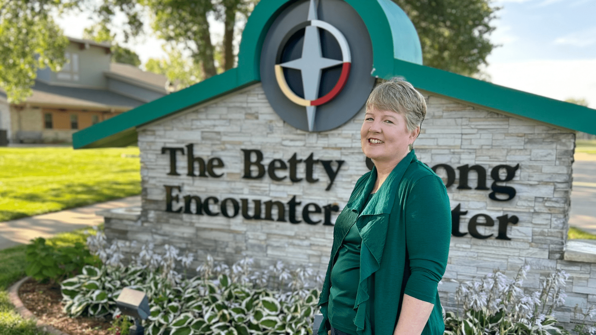 Sue Owens in front of the Betty Strong Encounter Center sign