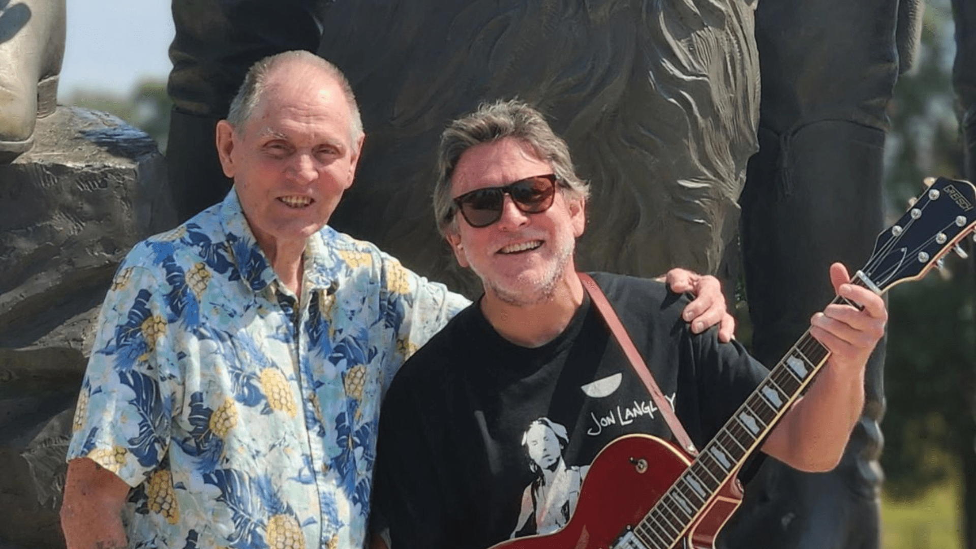 Older man with younger man holding a guitar.